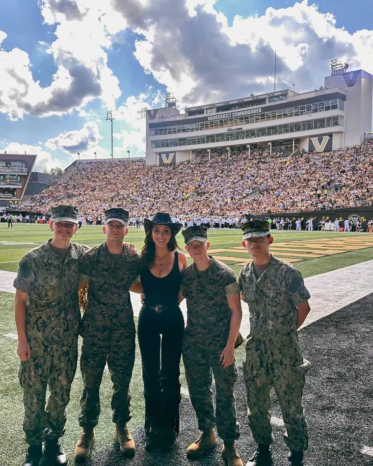 Crystal Marie on the field at a Vanderbilt Commodores game with five service members in uniform, a full stadium behind them