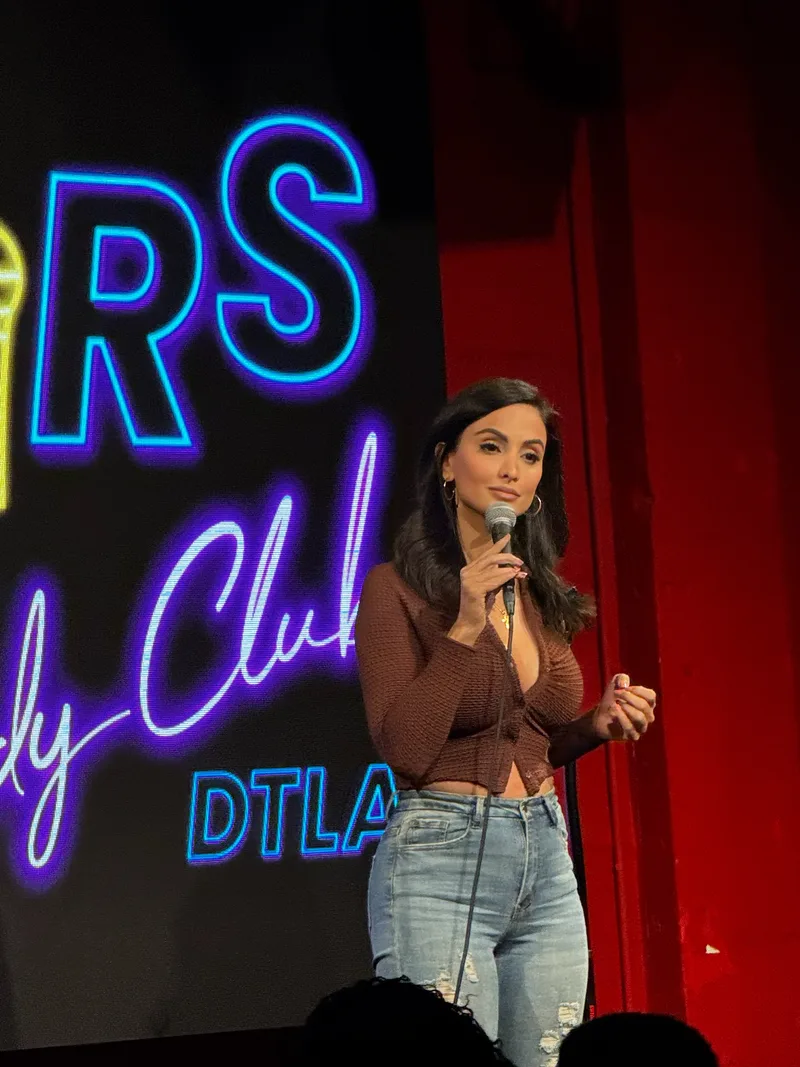 On stage with a microphone under the neon of a Downtown Los Angeles comedy club
