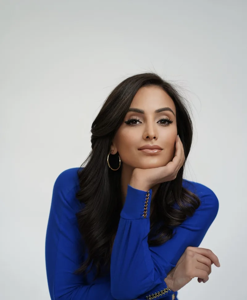 Studio portrait in a blue top, hand resting at her cheek